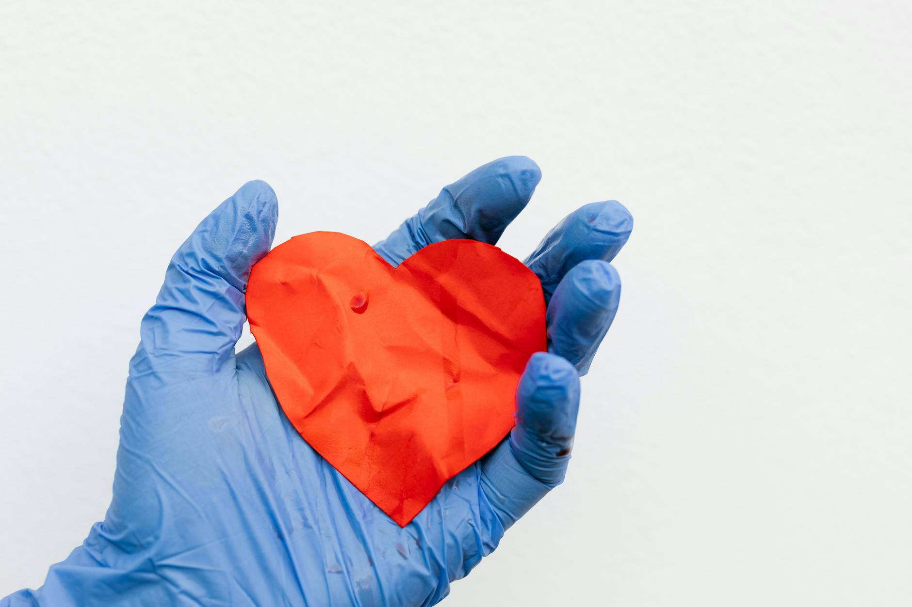 a person wearing latex gloves holding a heart cutout